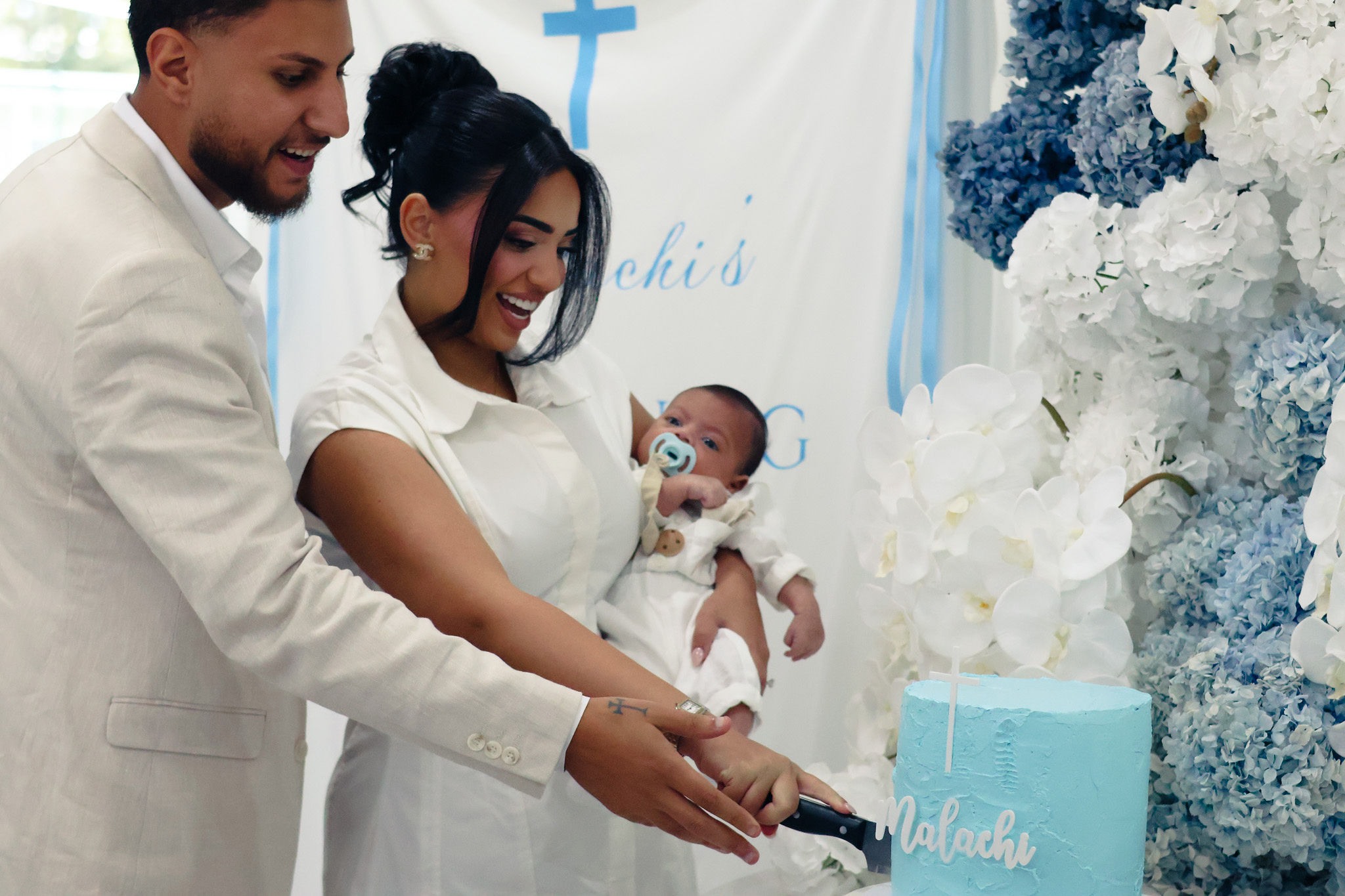 Parents cutting the christening cake while holding their baby