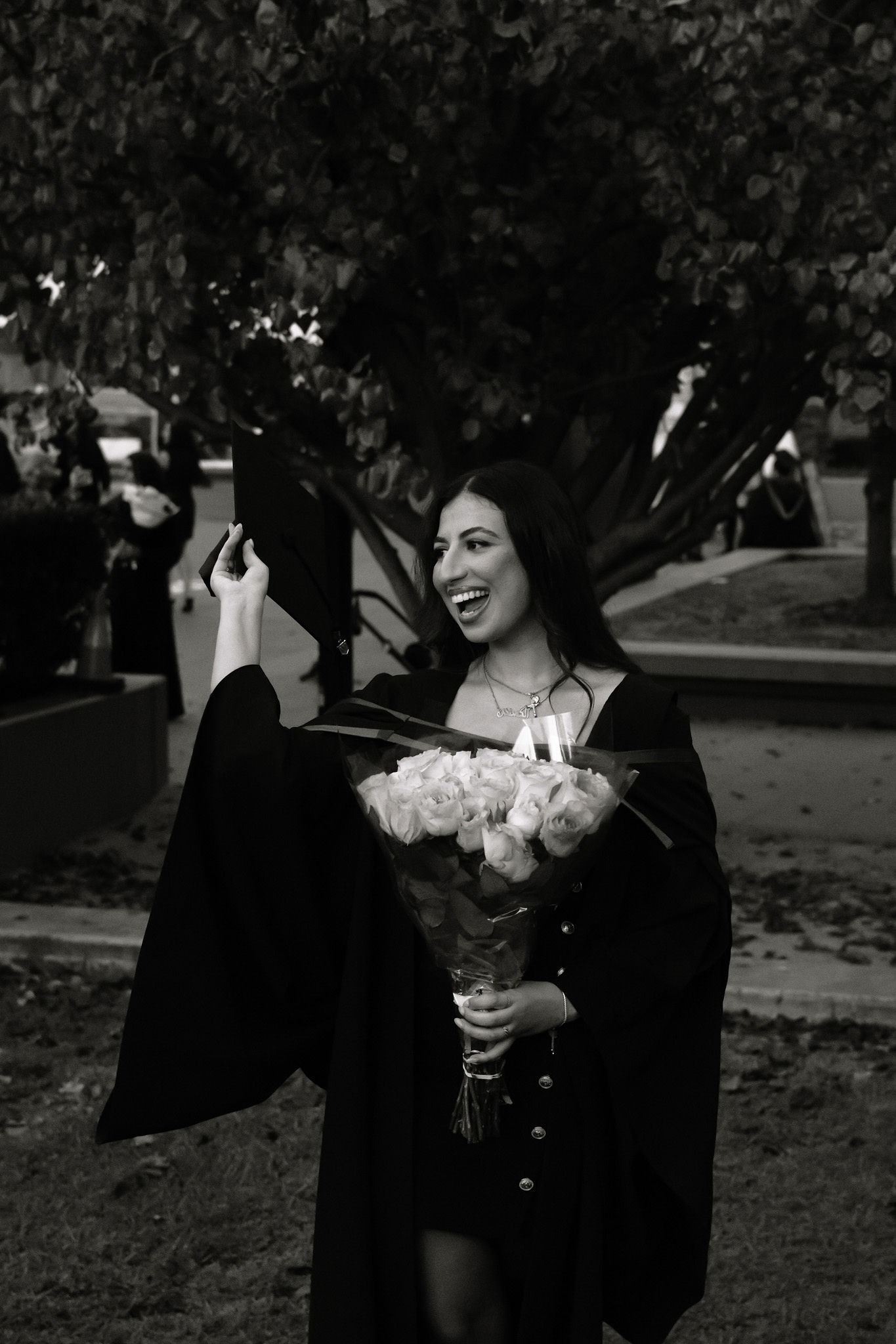 Black and white graduate laughing while holding flowers and her cap