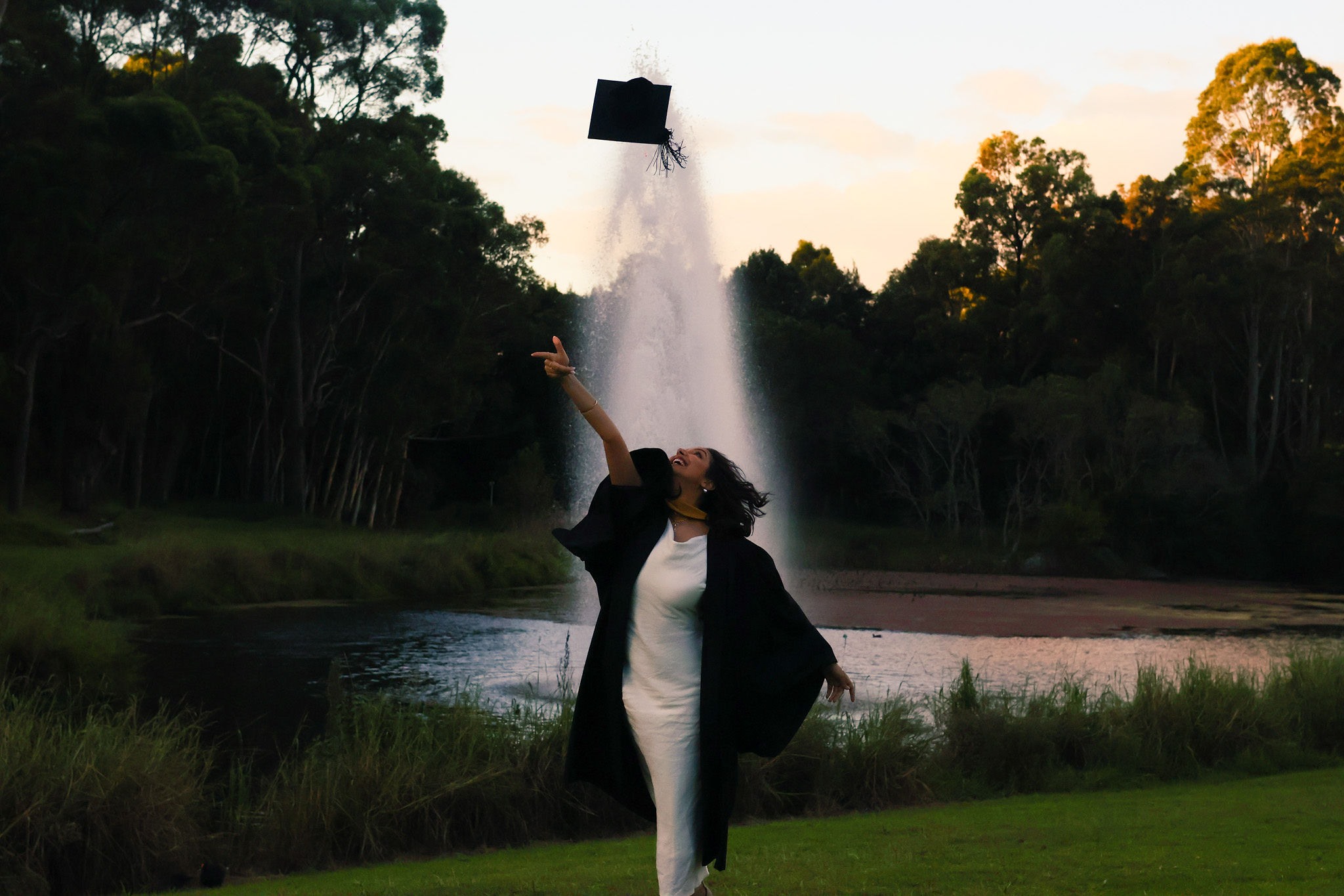 Graduate throwing her cap in front of a fountain
