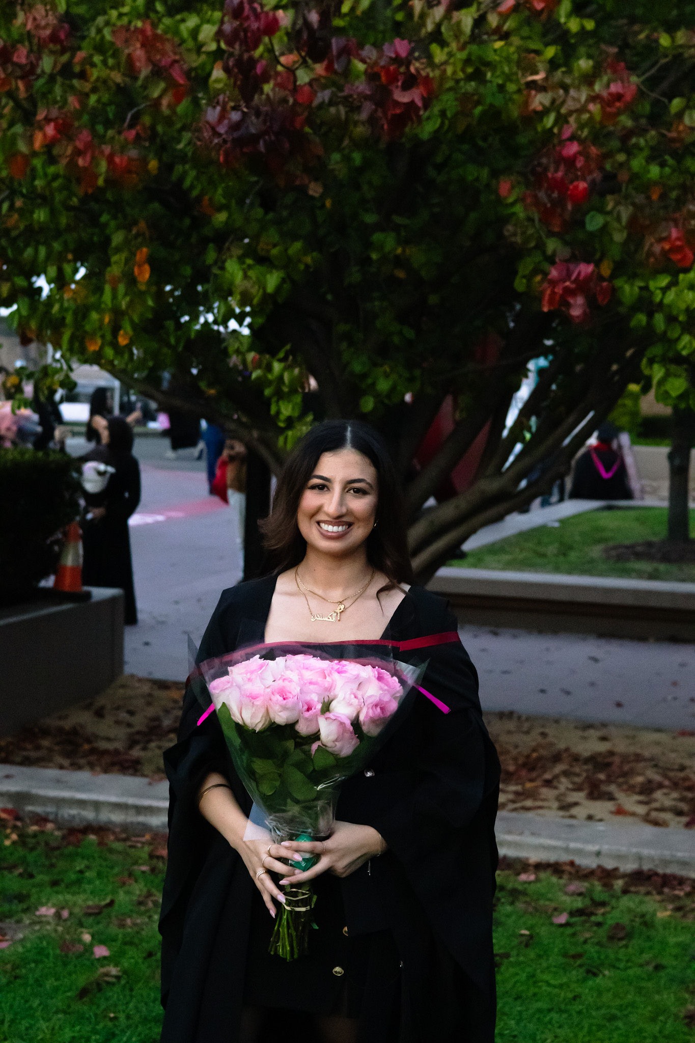 Graduate holding pink flowers beneath a tree