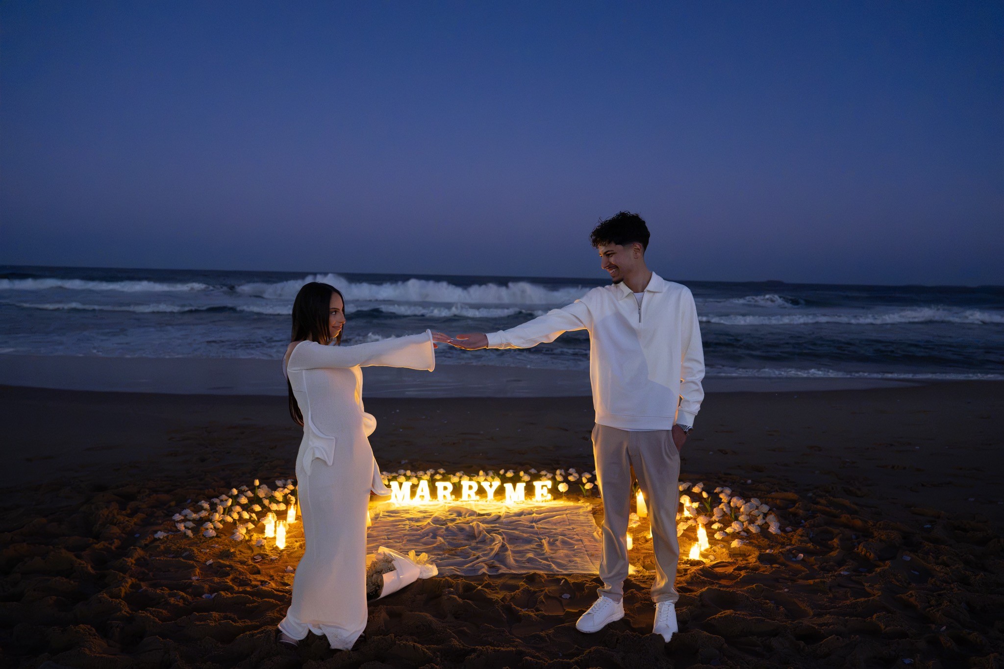 Couple holding hands in front of an illuminated marry me display