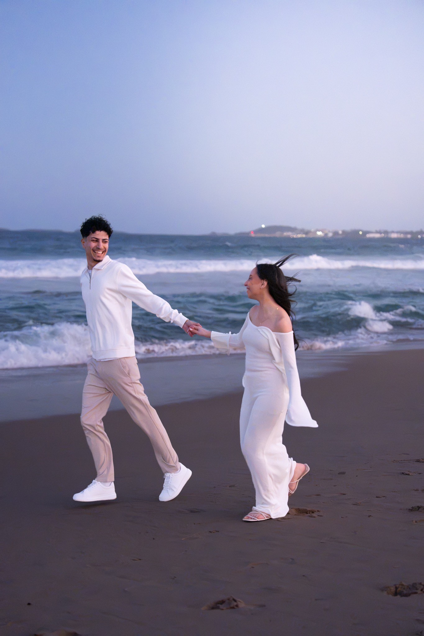 Newly engaged couple running together along the beach