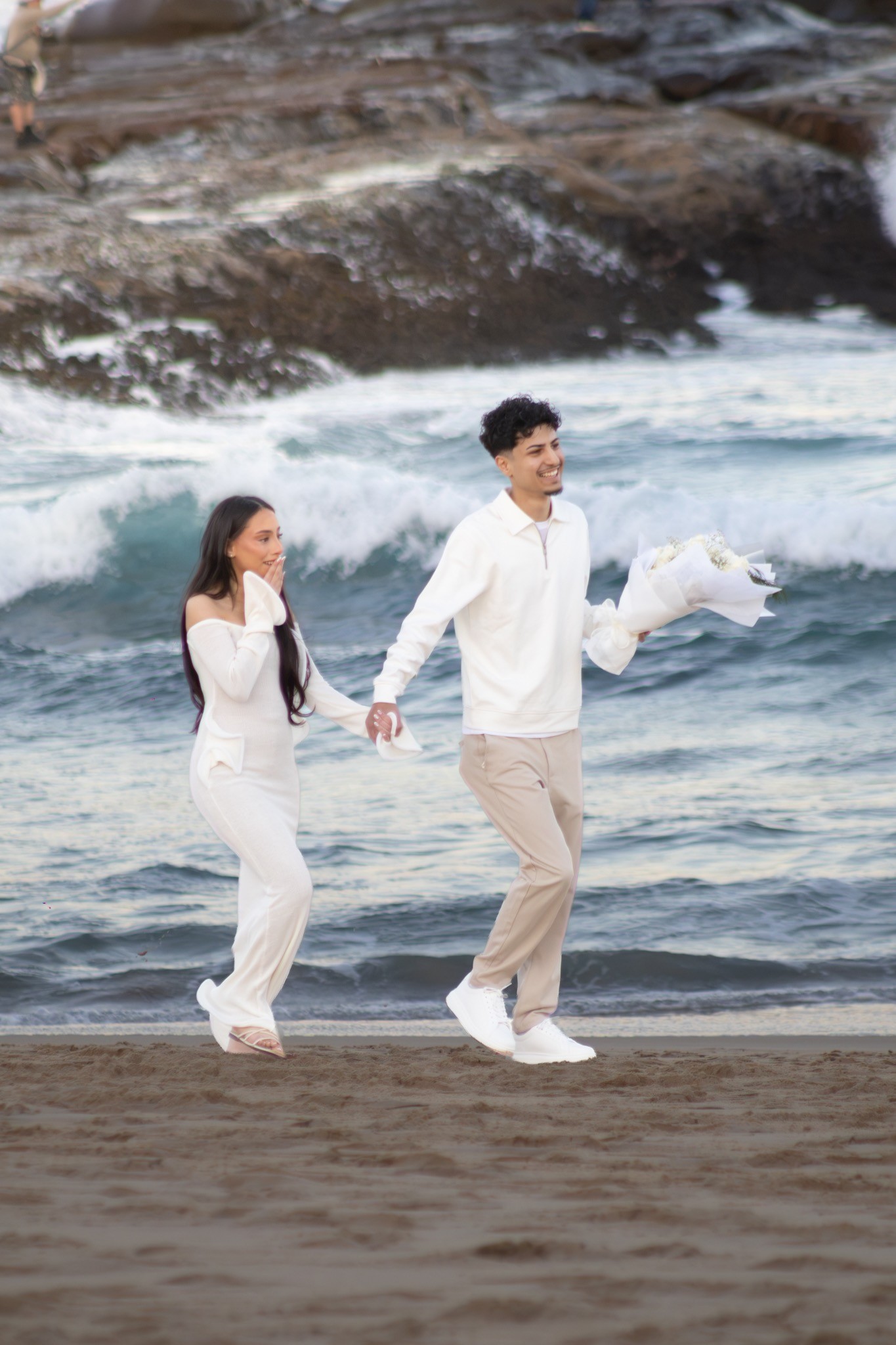 Newly engaged couple walking along the beach with flowers