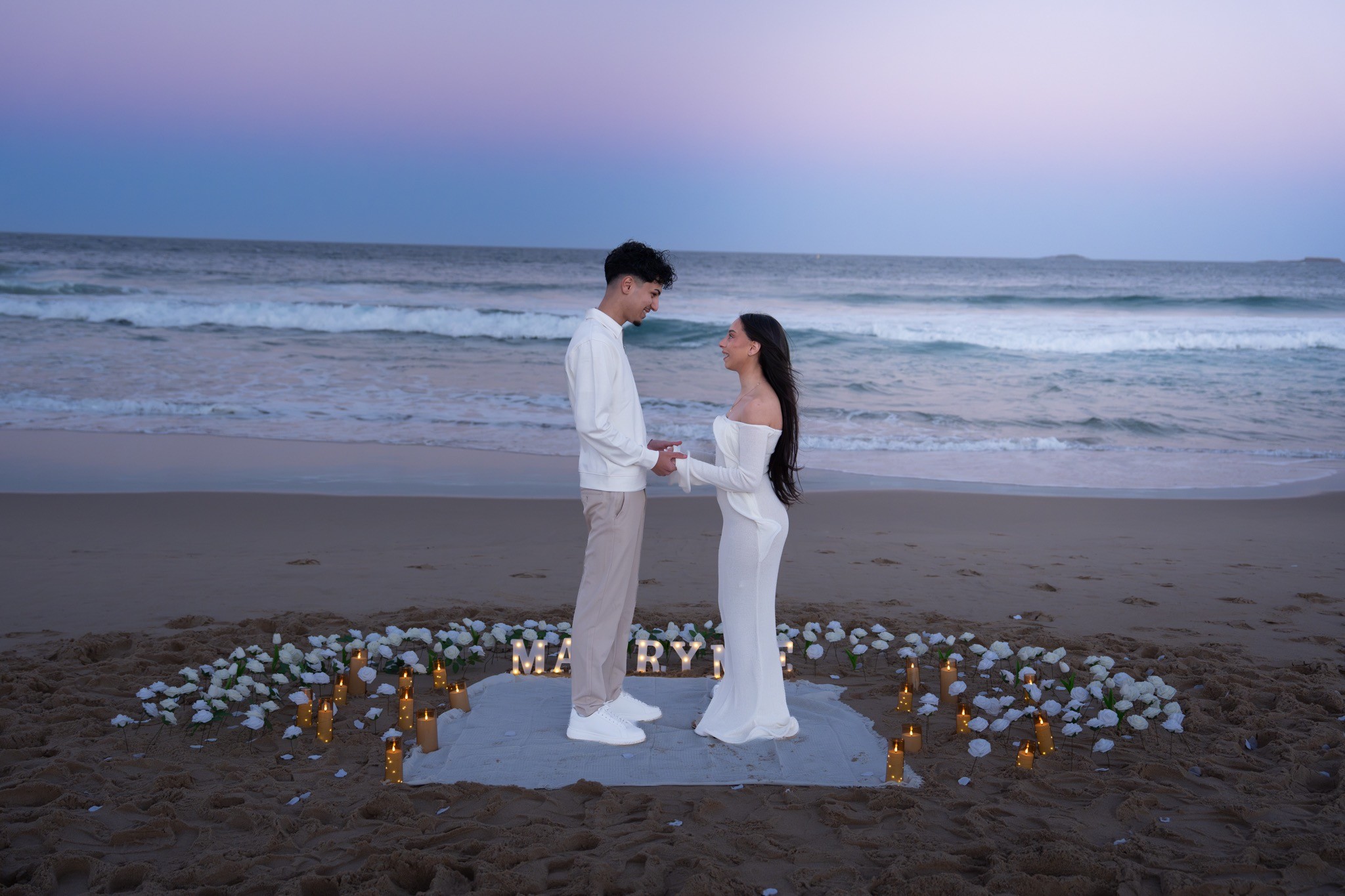 Couple standing inside a candlelit beach proposal setup